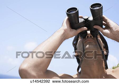 Young man looking through binoculars View Large Photo Image Stock Image - Young man looking through binoculars. Fotosearch