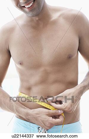 Young man measuring waist (midsection) View Large Photo Image Stock Photo - Young man measuring waist (midsection). Fotosearch