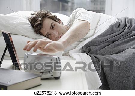 Stock Image - Young man switching alarm clock off. Fotosearch
