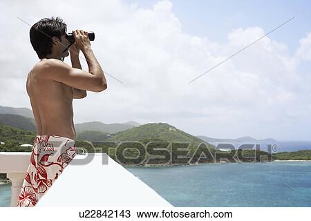 Stock Image - Young man using binoculars at seaside, St. John, US Virgin Islands, USA. Fotosearch