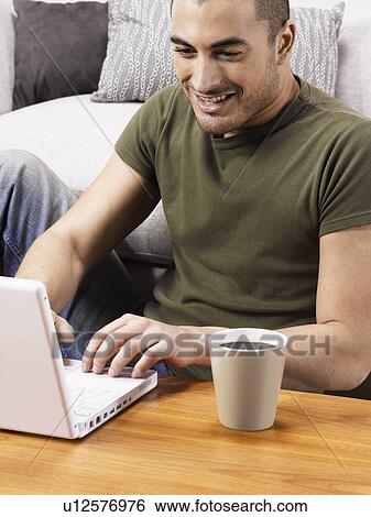 Young man using laptop on coffee table View Large Photo Image Stock Photograph - Young man using laptop on coffee table. Fotosearch