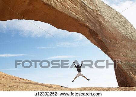 Stock Image - Man jumping under red rock. Fotosearch