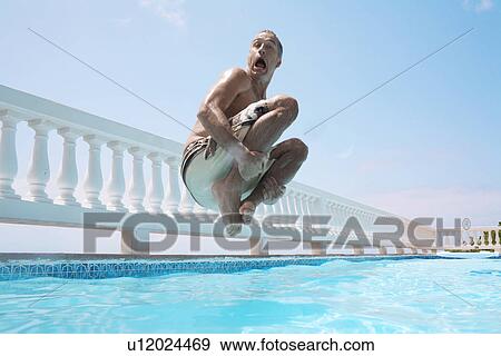 Stock Photo - Mid adult man jumping into swimming pool. Fotosearch