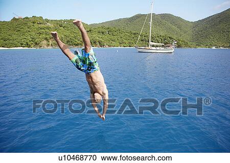 Stock Image - Mid adult man jumping into water, St. John, US Virgin Island, USA. Fotosearch