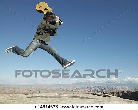 Mid adult man with acoustic guitar jumping, rock strata in background View Large Photo Image Stock Photograph - Mid adult man with acoustic guitar jumping, rock strata in background. Fotosearch