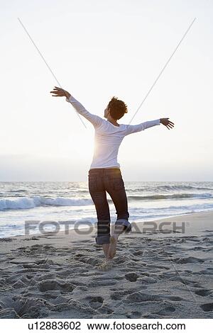 Stock Image - Mid adult woman running on beach. Fotosearch