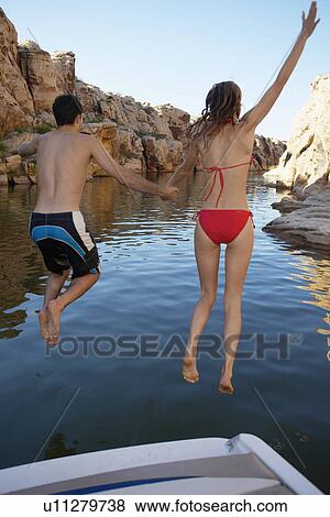 Stock Photo - Young couple jumping from motorboat to lake (rear view). Fotosearch
