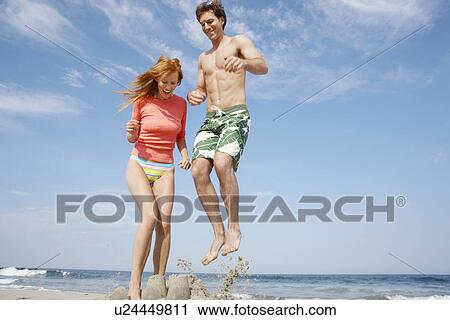 Stock Image - Young couple jumping on sandcastle. Fotosearch