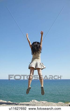 Stock Image - Young Woman Jumping by Sea. Fotosearch