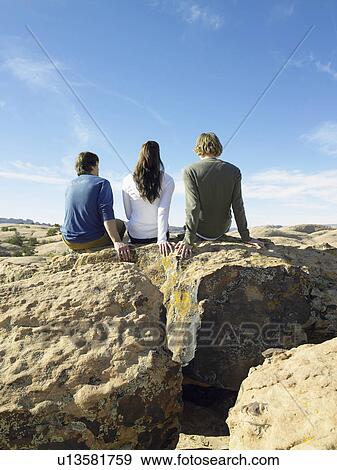 Three friends sitting on rocks, rear view View Large Photo Image Stock Photo - Three friends sitting on rocks, rear view. Fotosearch