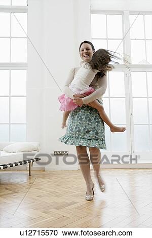 Stock Image - Mother carrying daughter in living room. Fotosearch