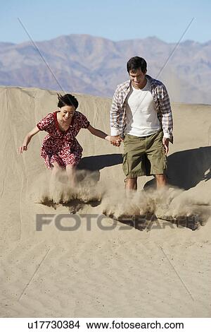 Picture - Couple sliding down on sand dune. Fotosearch