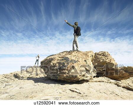 Stock Image - Man and woman standing on boulders and waving to each other. Fotosearch