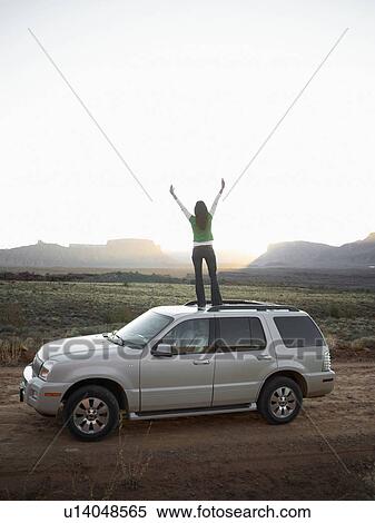 Stock Photography - Woman standing on roof of car, arms outstretched, rear view, Moab, Utah, USA. Fotosearch