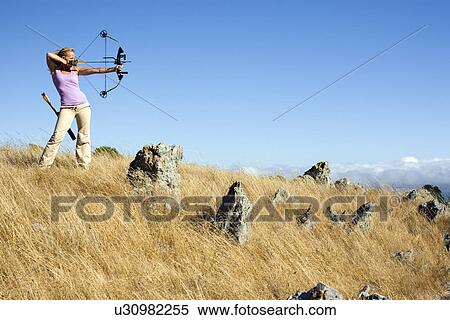 Stock Photography - Young woman arrow shooting in field. Fotosearch