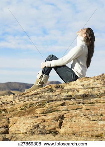 Young woman sitting on rocky hill, low angle view View Large Photo Image Stock Photo - Young woman sitting on rocky hill, low angle view. Fotosearch