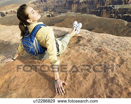Young woman with backpack sitting on cliff, rear view View Large Photo Image Stock Photo - Young woman with backpack sitting on cliff, rear view. Fotosearch