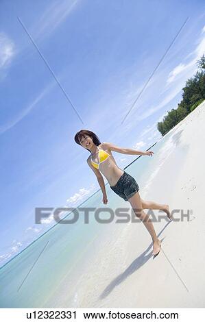 Stock Image - Portrait of a young woman walking on beach, smiling, Saipan, USA . Fotosearch