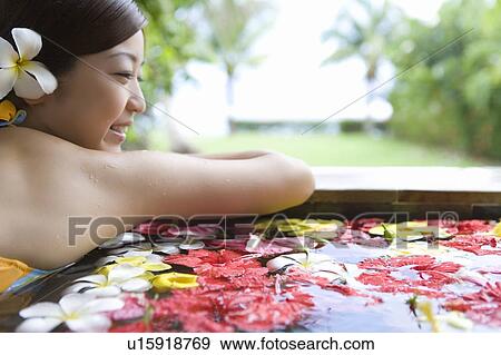 Stock Photo - Young woman in a bath full of flowers, Saipan, Rear View. Fotosearch