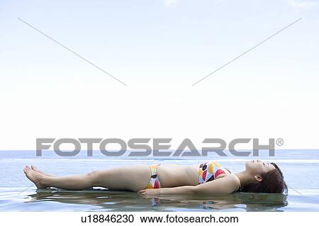 Stock Image - Young woman in a bikini lying on water, Saipan. Fotosearch