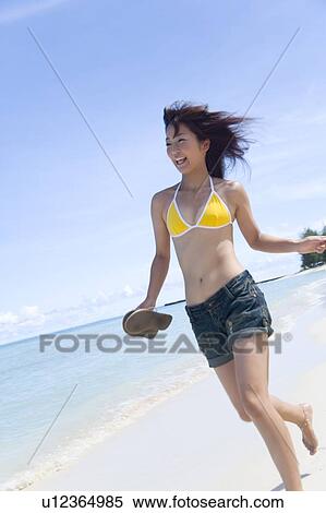 Stock Photography - Young woman running on beach, holding sandals, Saipan, USA . Fotosearch