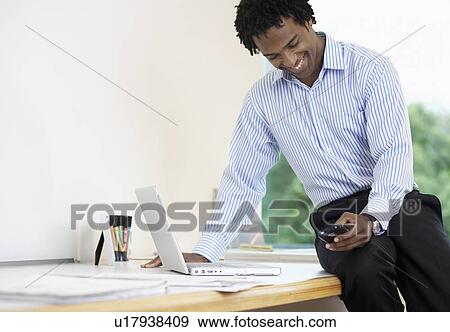 Stock Photo - Businessman with laptop using PDA. Fotosearch