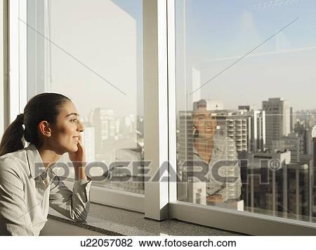 Stock Image - Businesswoman talking on phone by window, Sao Paolo, Brazil. Fotosearch