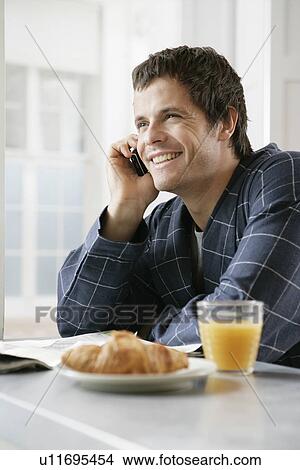 Picture - Mid adult man talking on the phone at breakfast table. Fotosearch