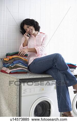 Mid adult woman sitting on washing machine and talking on phone View Large Photo Image Stock Photography - Mid adult woman sitting on washing machine and talking on phone. Fotosearch