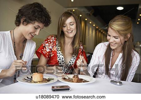 Stock Image - Teenage girls eating deserts in restaurant. Fotosearch