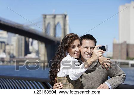 Picture - Couple taking photograph of themselves, Brooklyn Bridge in background, New York City, New York, USA. Fotosearch