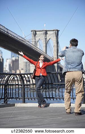 Stock Image - Man photographing woman near Brooklyn Bridge, New York City, New York, USA. Fotosearch