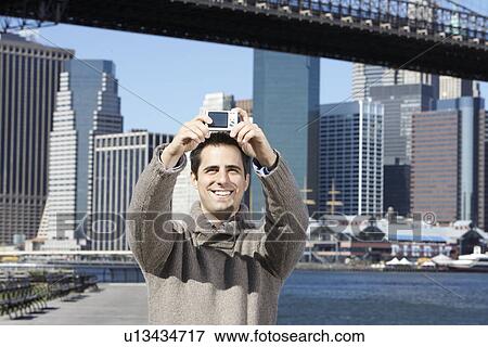 Stock Photo - Man taking photograph of himself with skyline in background, New York City, New York, USA. Fotosearch