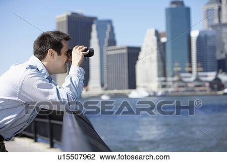 Stock Image - Man using binoculars, Manhattan in background, New York City, New York, USA. Fotosearch
