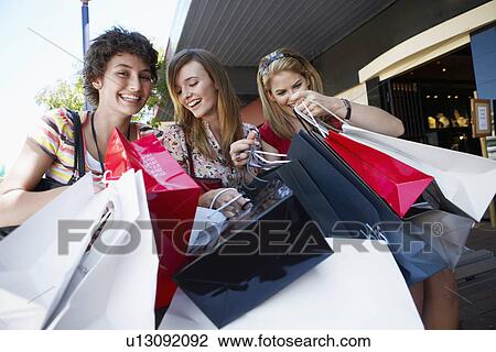 Stock Image - Three teenage girls looking at their shopping bags. Fotosearch