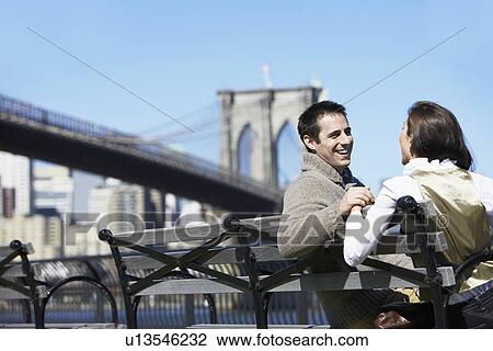 Young couple sitting on bench near Brooklyn Bridge, Brooklyn, New York City, New York, USA View Large Photo Image Stock Image - Young couple sitting on bench near Brooklyn Bridge, Brooklyn, New York City, New York, USA. Fotosearch