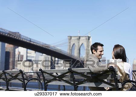 Young couple sitting on bench near Brooklyn Bridge, Brooklyn, New York City, New York, USA View Large Photo Image Stock Photo - Young couple sitting on bench near Brooklyn Bridge, Brooklyn, New York City, New York, USA. Fotosearch