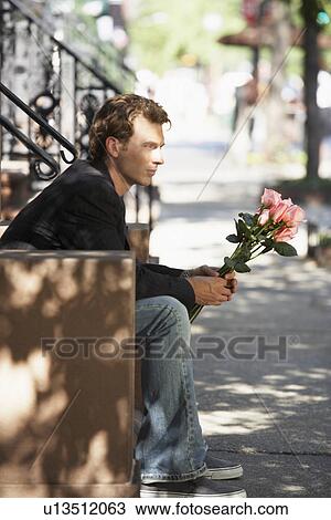 Stock Image - Young man with bunch of roses sitting on steps. Fotosearch