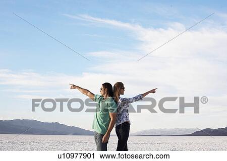 Couple standing back to back and pointing to opposite directions by lake View Large Photo Image Stock Image - Couple standing back to back and pointing to opposite directions by lake. Fotosearch