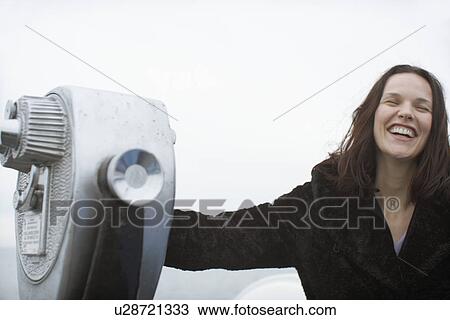 Stock Image - Young woman laughing by coin-operated binoculars. Fotosearch