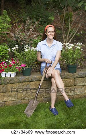 Stock Photo - Female gardener sitting on brick wall (portrait). Fotosearch