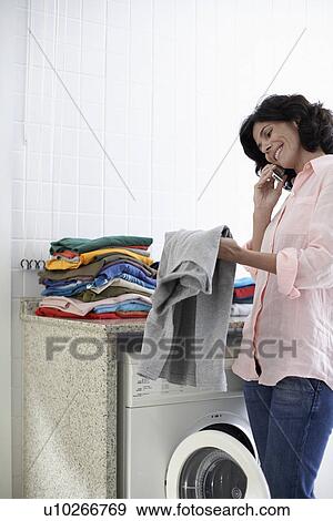 Stock Photo - Mid adult woman on phone in laundry room. Fotosearch