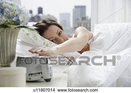 Picture - Mid adult woman reaching for alarm clock. Fotosearch