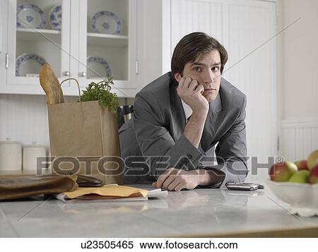 Stock Photography - Young businessman with bag of groceries leaning on kitchen counter. Fotosearch