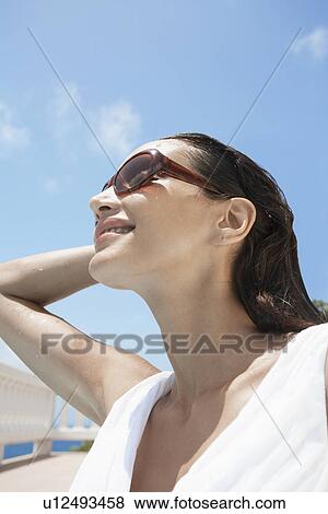 Stock Photo - Young woman wearing sunglasses (low angle view). Fotosearch