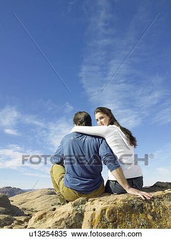 Stock Photography - Couple sitting on rock, portrait, rear view. Fotosearch