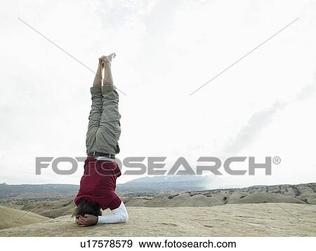 Stock Photo - Man standing on head, rock strata in background. Fotosearch