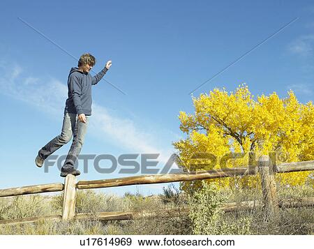 Stock Photo - Man standing on pole of fence, low angle view. Fotosearch