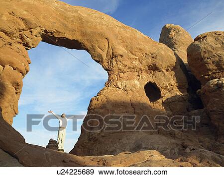 Stock Photo - Man standing under arched rock with arms raised. Fotosearch