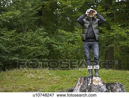 Stock Photo - Man Using Binoculars on Tree Stump. Fotosearch